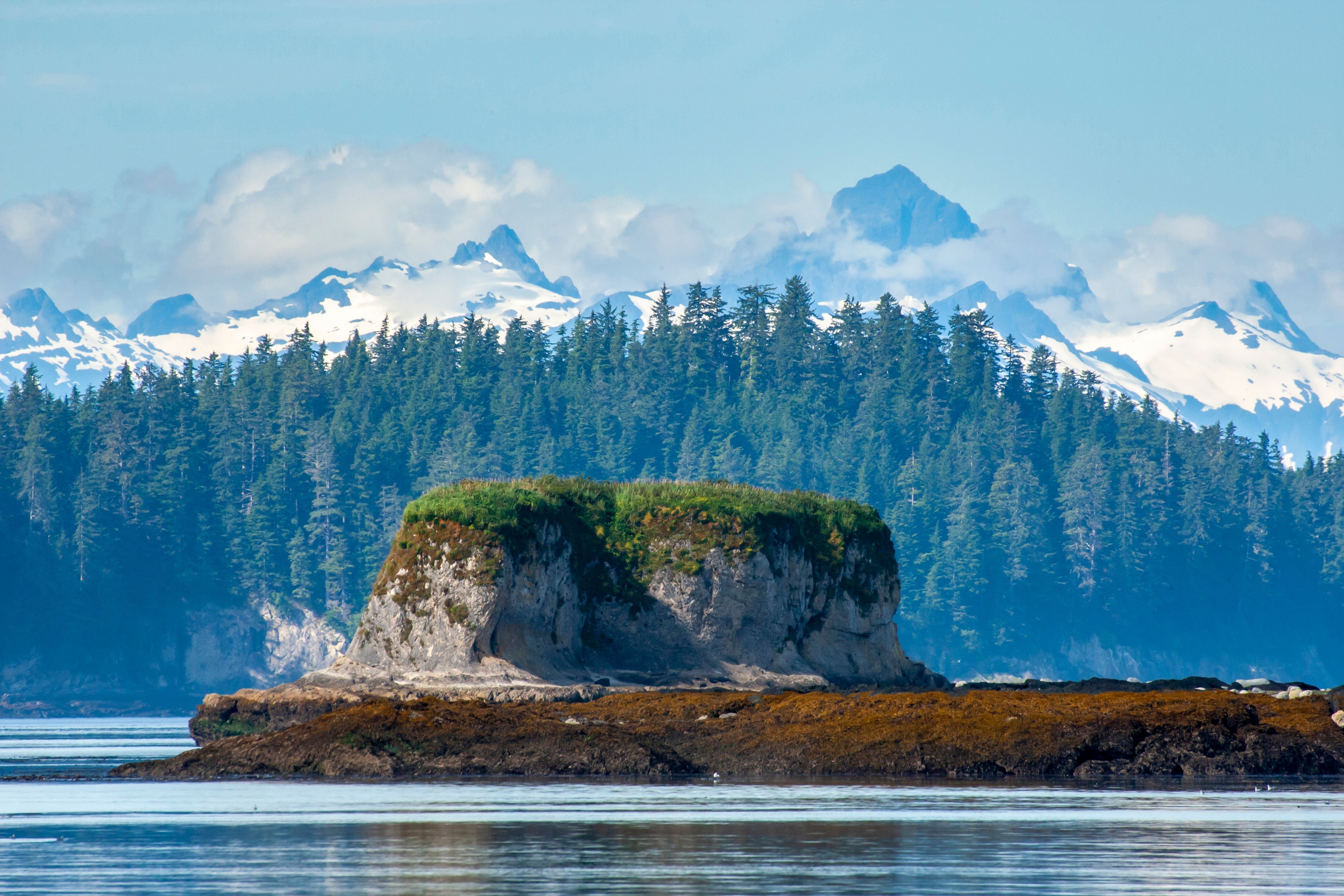 Kruzof Adventure excursion showcasing rugged Alaska coastline, forested sea stack, and snow-capped mountain peaks in pristine wilderness scenery.