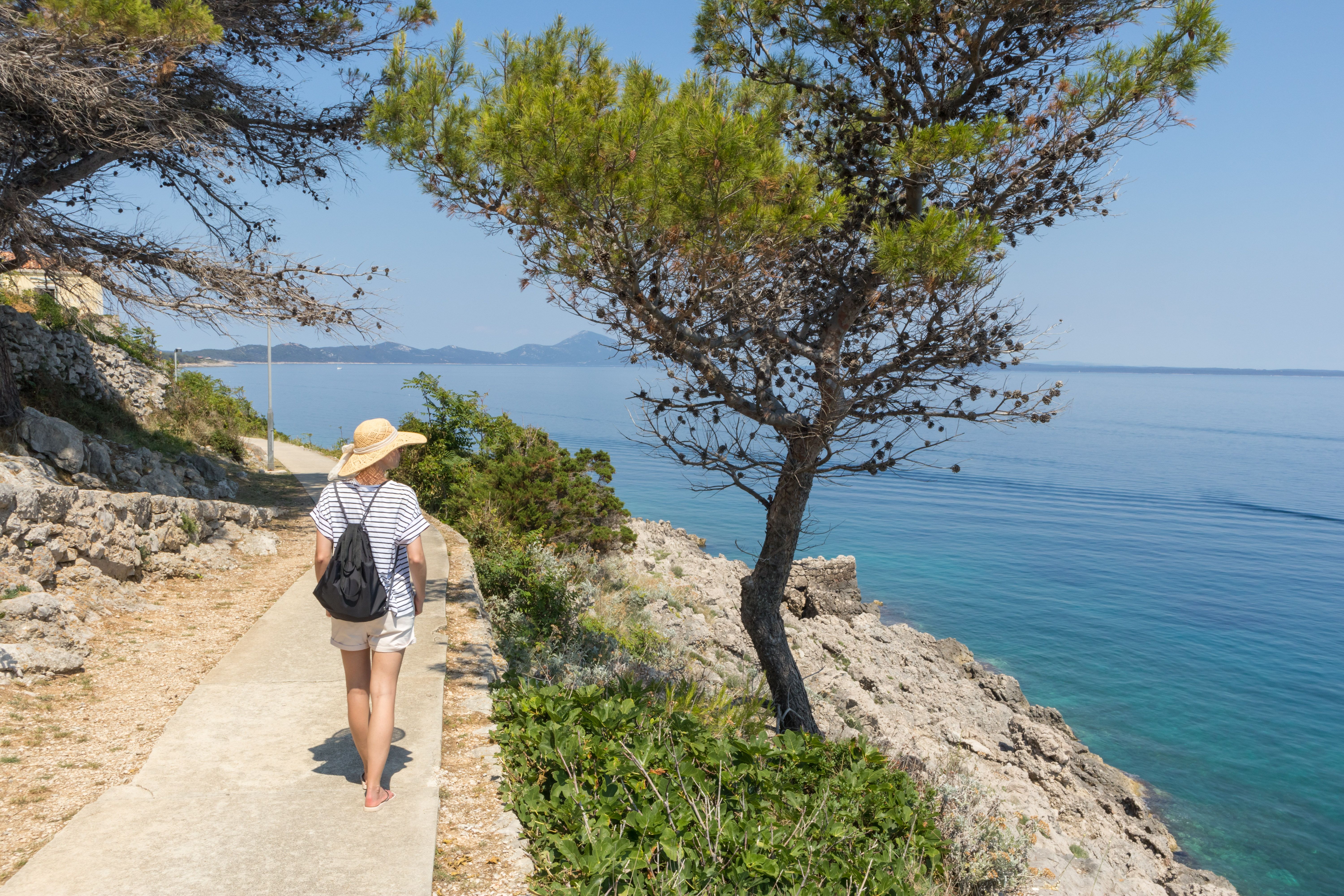 Scenic coastal hiking trail on Hvar Island with a traveler overlooking the crystal-clear Adriatic Sea, showcasing Croatia's natural beauty and Mediterranean coastline.