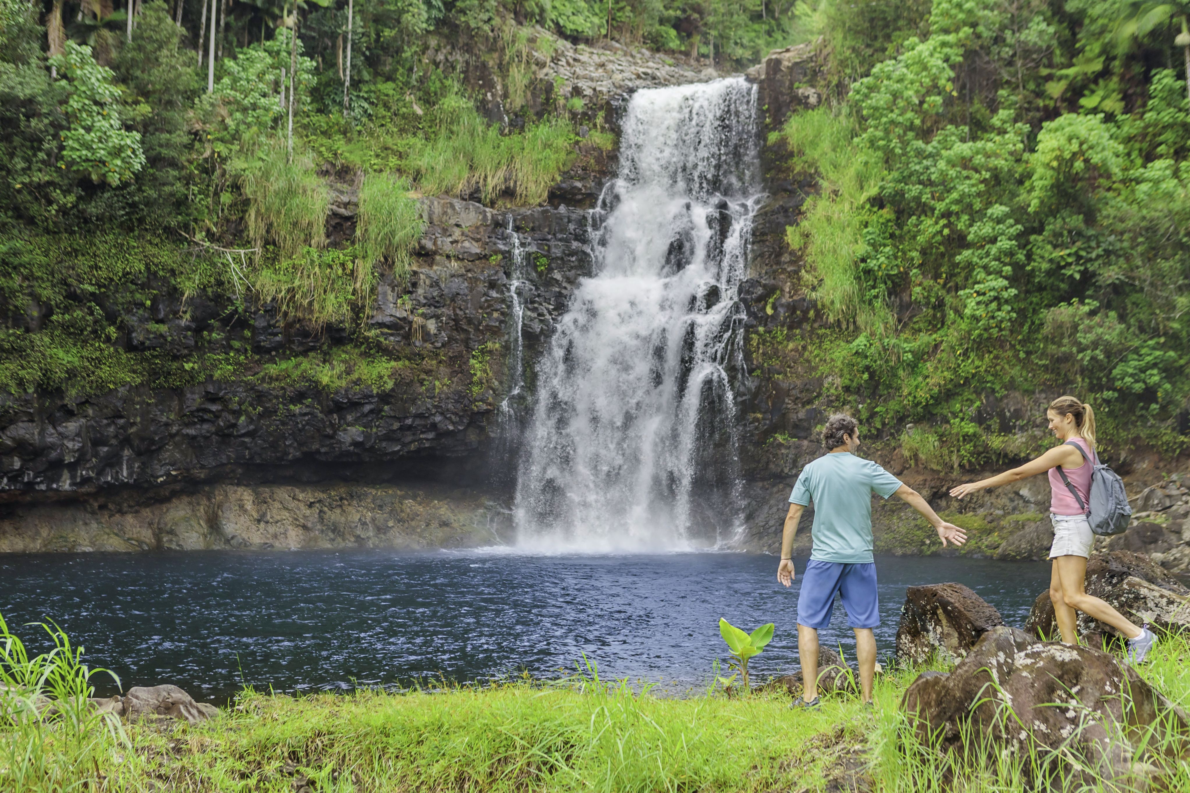 Hikers explore a lush Hawaiian rainforest waterfall and swimming pool, highlighting a scenic Hawaii shore excursion and tropical island adventure.