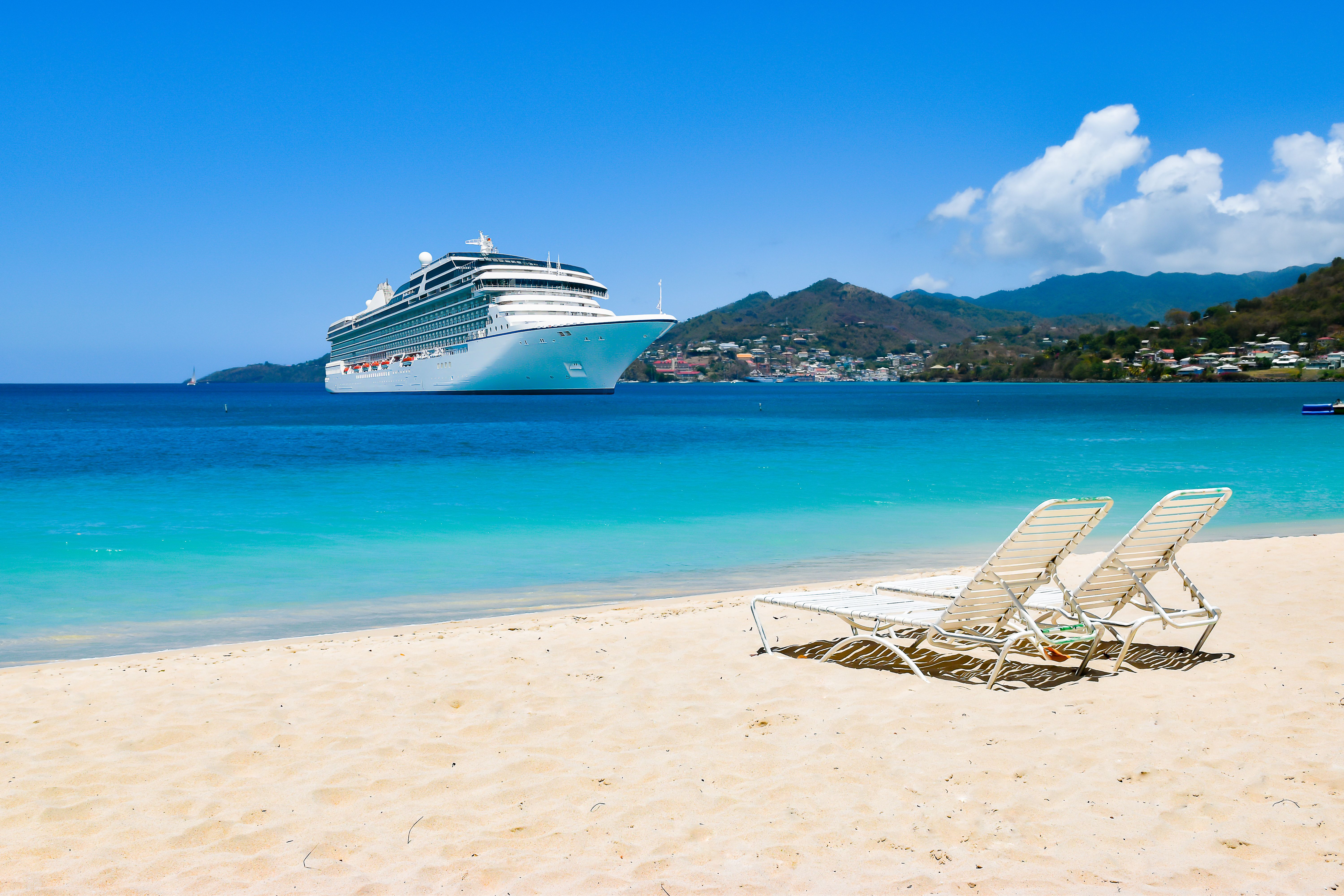 Celebrity Cruises ship sailing in turquoise Caribbean waters beside a white sand beach with lounge chairs and a lush tropical island backdrop.