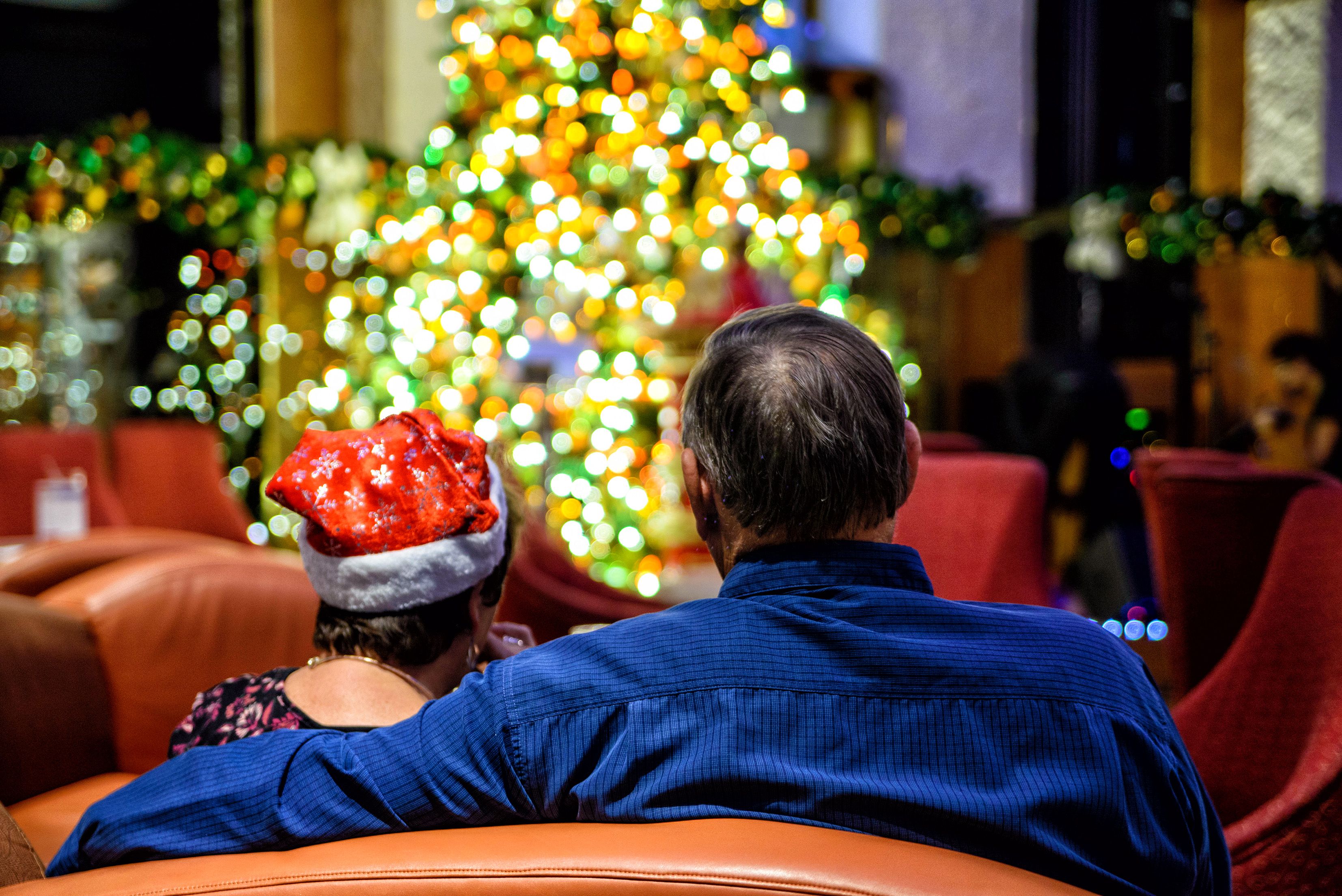 Cruise passengers relax in a festive lounge beside a glowing Christmas tree, enjoying holiday decorations and a cozy atmosphere at sea.