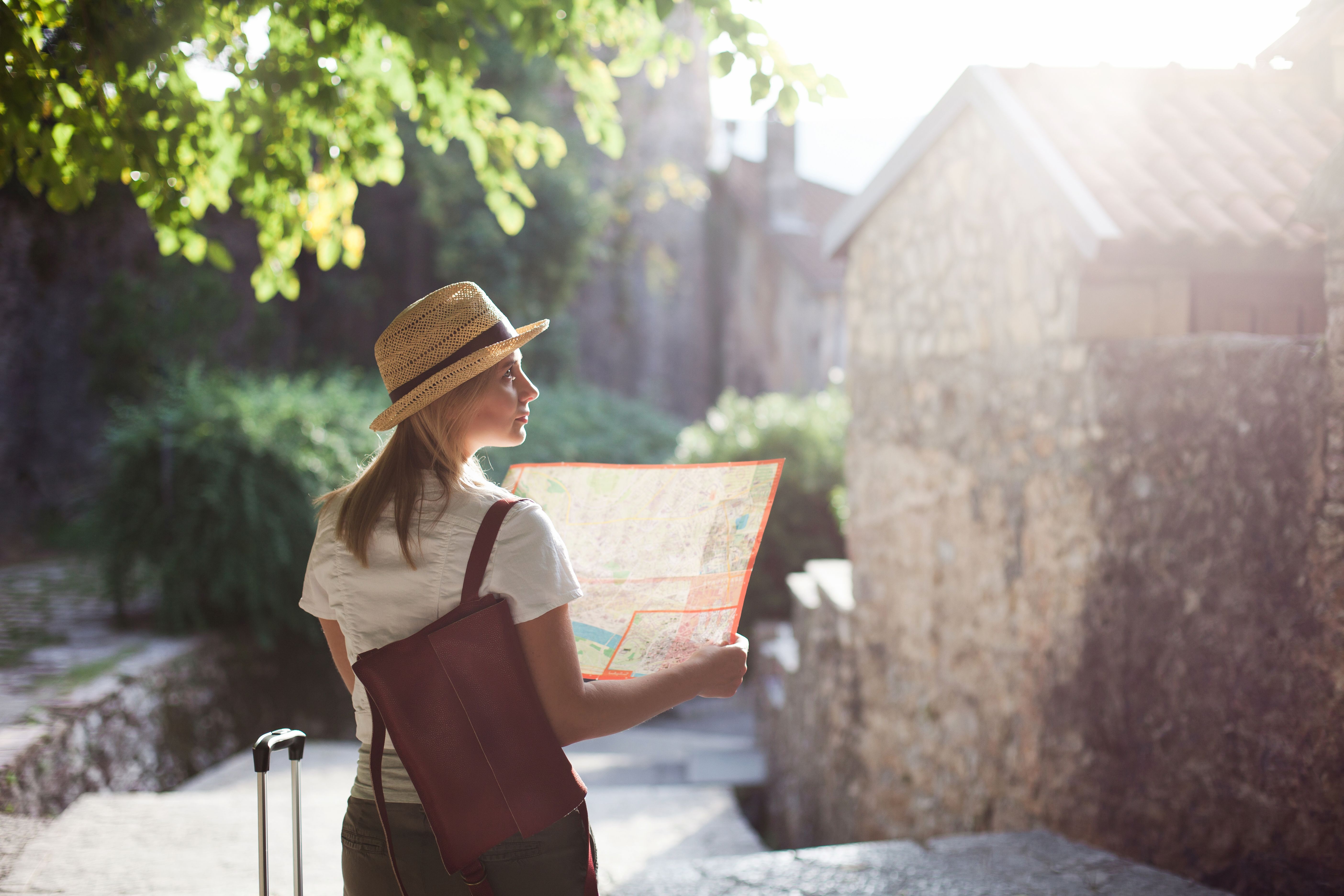 Solo female traveler exploring a historic destination with a city map and luggage, ideal for independent cruise shore excursions and sightseeing.