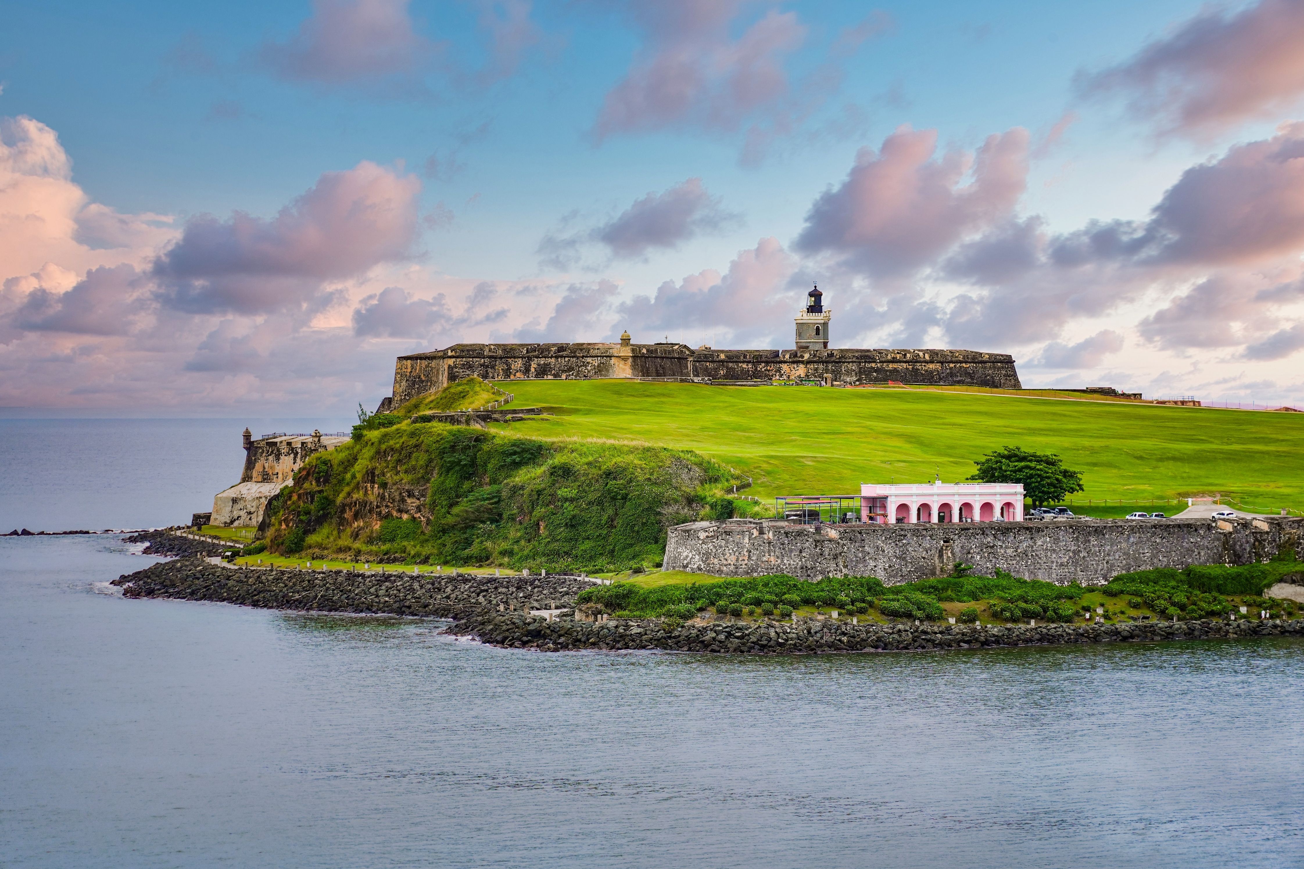 Historic Castillo San Felipe del Morro fortress overlooking the Caribbean Sea in San Juan, Puerto Rico, with lush green lawns and pastel sunset clouds.