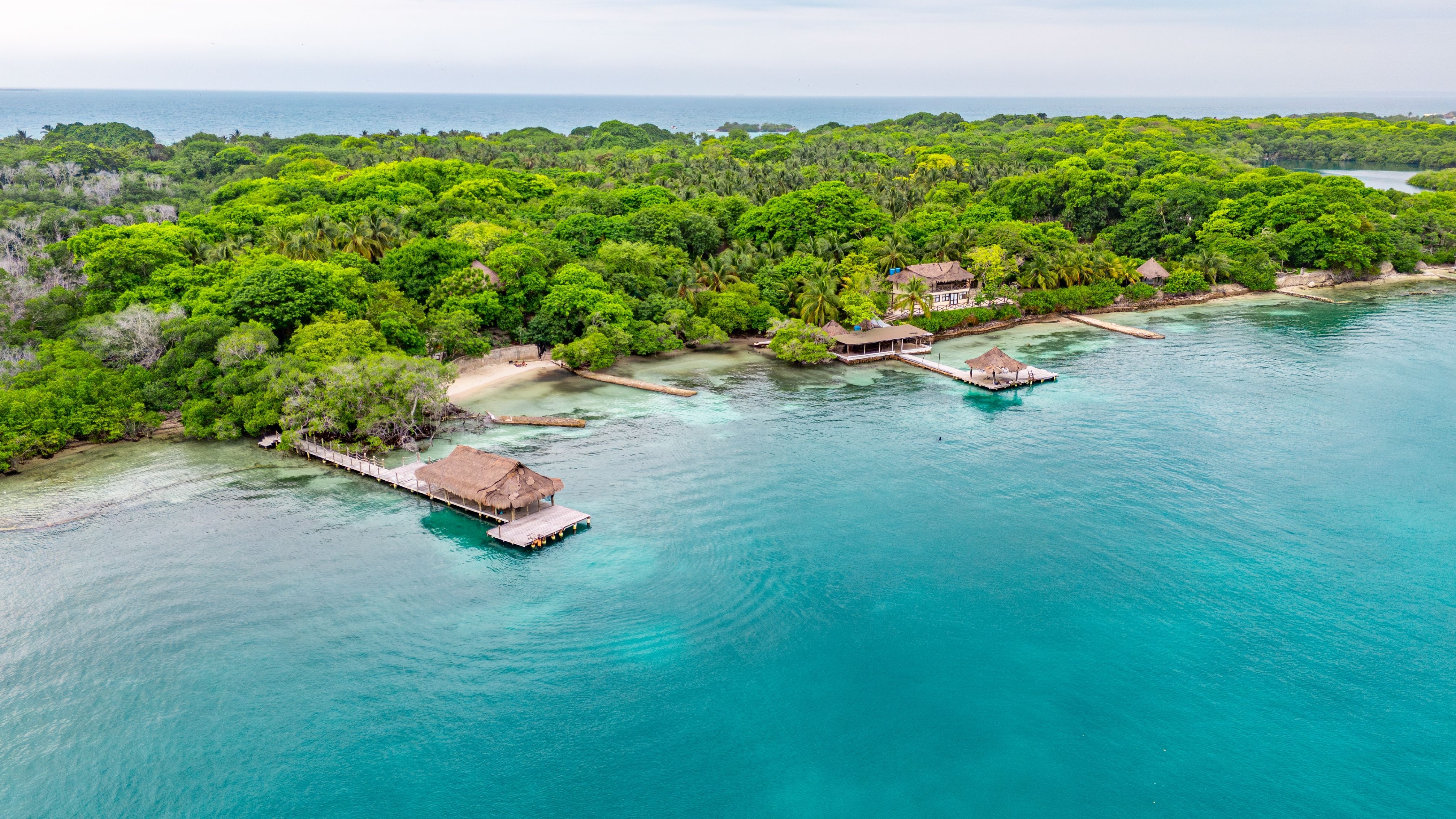 Aerial view of the Rosario Islands near Cartagena, Colombia, featuring turquoise Caribbean waters, lush tropical forests, sandy beaches and thatched-roof piers.
