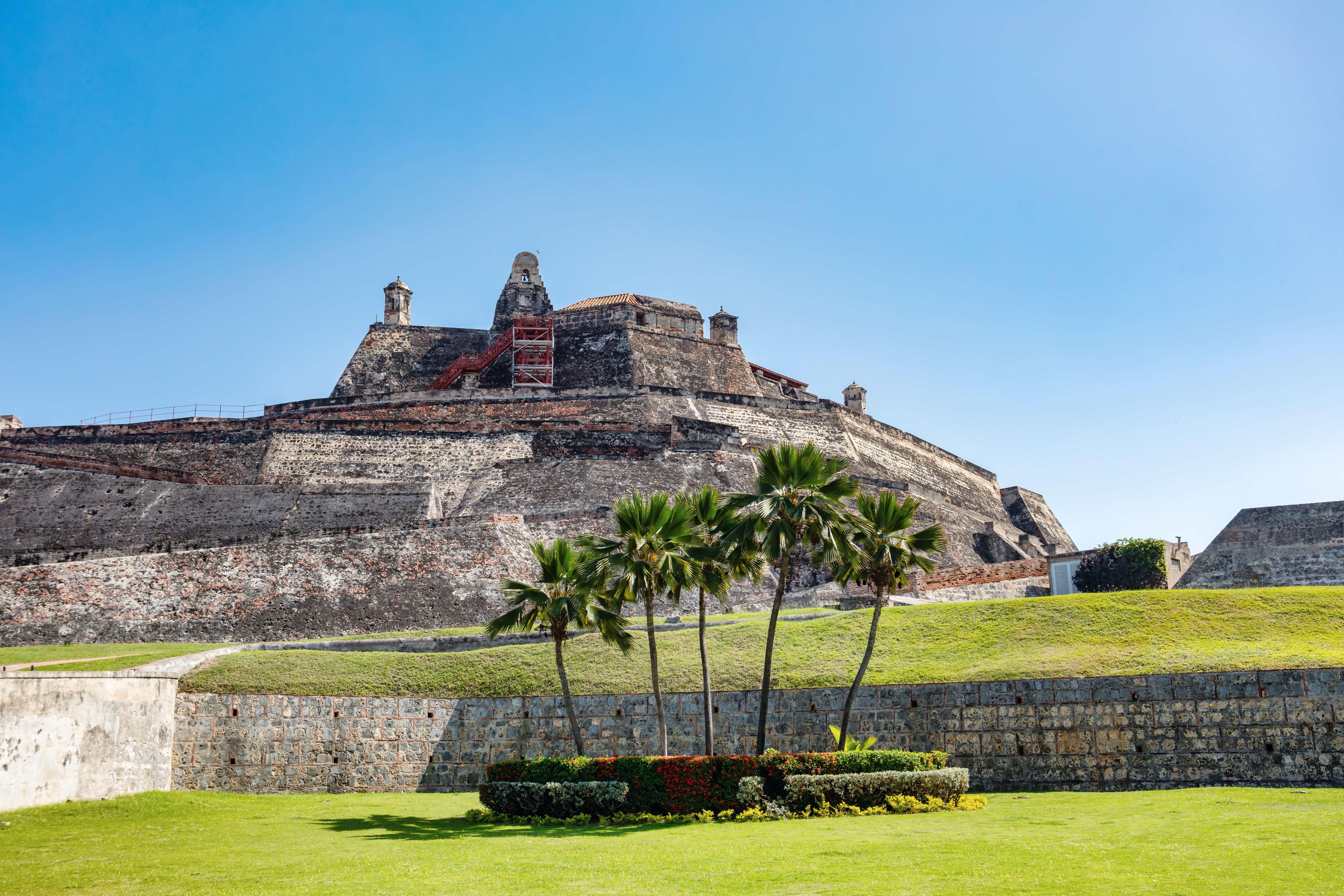 Historic Castillo San Felipe de Barajas fortress in Cartagena, Colombia, featuring massive stone walls, palm trees and green lawns beneath a clear blue Caribbean sky.