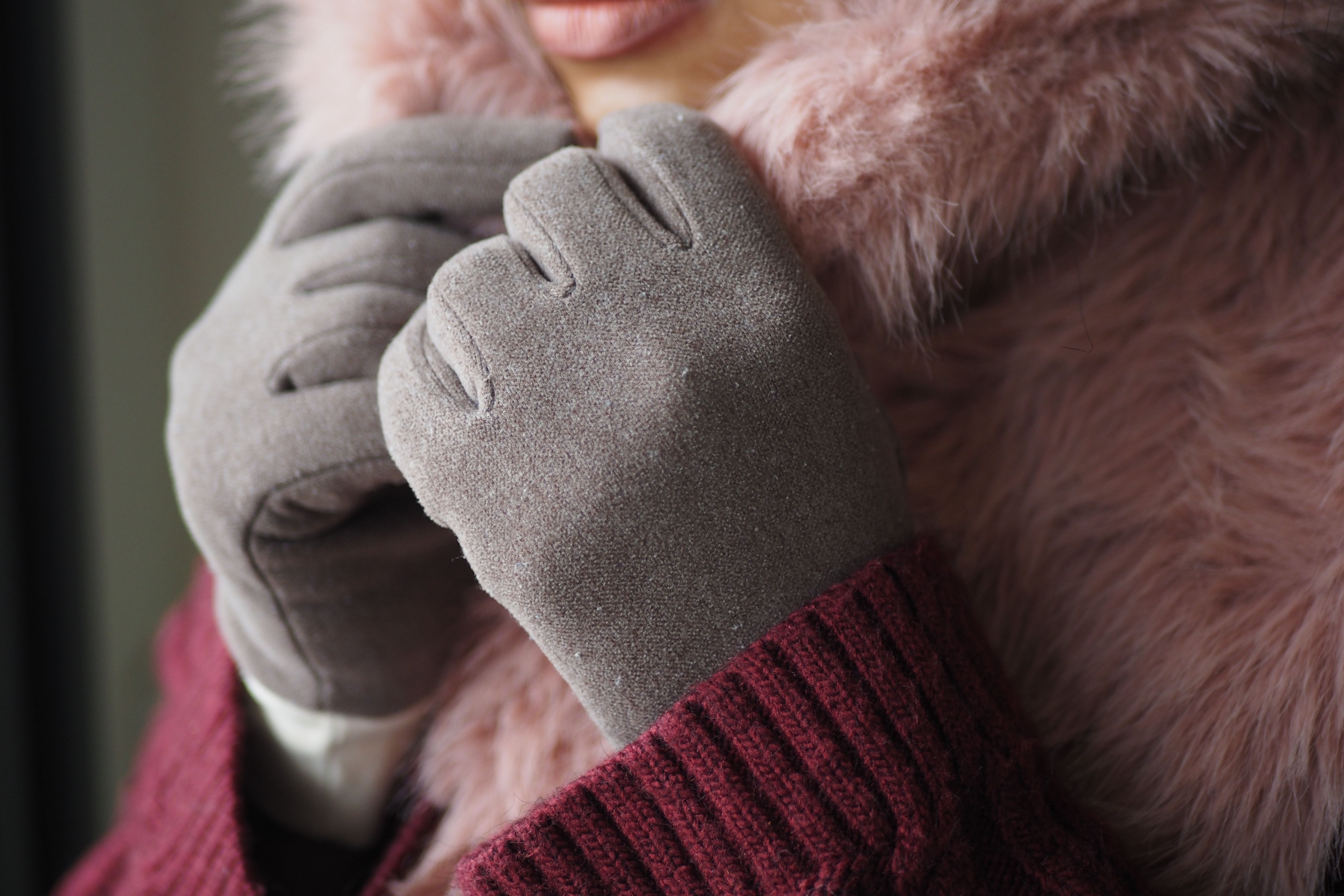 Close-up of gray winter gloves holding a fluffy pink collar above burgundy knit sleeves.