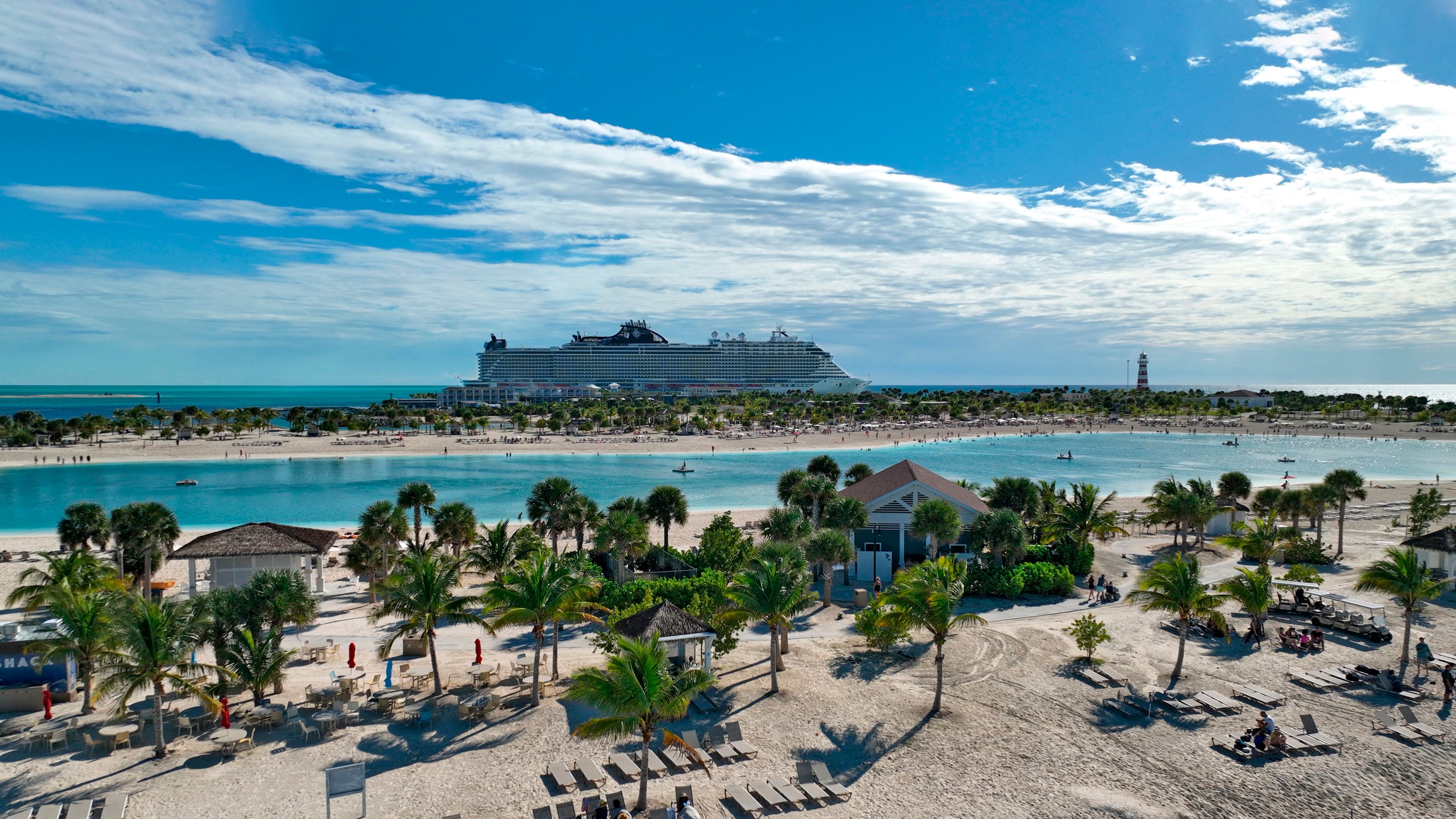 Panoramic view of MSC Cruises' Ocean Cay Marine Reserve in the Bahamas, featuring beachfront cabanas, palm trees, turquoise lagoons and a docked cruise ship.