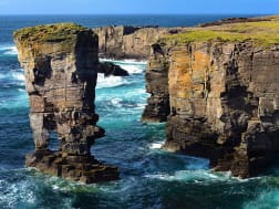 Steile Klippen und freistehende Felsnadel in rauer Brandung an der K&uuml;ste der Britischen Inseln