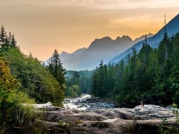 Flusslauf inmitten dichter W&auml;lder vor einer Bergkulisse im Abendlicht in Nordamerika