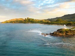Amber Cove, Dominikanische Republik &ndash; Wei&szlig;er Turm auf felsiger Kapspitze &uuml;ber ruhigem Strand und gr&uuml;nem Hang