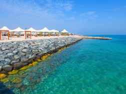 Sir Bani Yas, VAE &ndash; K&uuml;stenpromenade mit Zeltd&auml;chern und glasklarem Wasser unter blauem Himmel