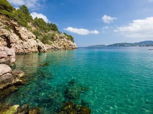 Baie m&eacute;diterran&eacute;enne ensoleill&eacute;e avec eau bleue cristalline et c&ocirc;te rocheuse.
