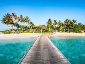Langer Holzsteg f&uuml;hrt zu tropischem Strand mit Palmen und t&uuml;rkisfarbenem Wasser
