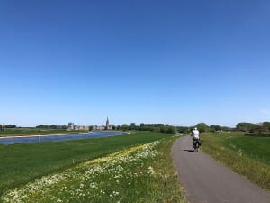 Radfahrer auf einem Deichweg entlang eines Flusses bei klarem Sommerhimmel