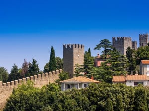 Koper, Slowenien &ndash; m&auml;chtige Stadtmauer mit Zinnen zwischen Zypressen