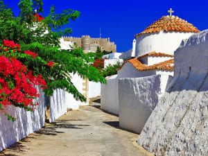 Patmos, Griechenland &ndash; Enge Gasse mit wei&szlig;er Kapelle und Blick auf die Johanniterfestung