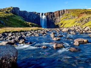 Sey&eth;isfj&ouml;r&eth;ur, Island &ndash; Majest&auml;tischer Wasserfall st&uuml;rzt zwischen gr&uuml;nen Felsen herab