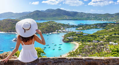 Frau im wei&szlig;en Kleid genie&szlig;t den Panoramablick &uuml;ber die Landschaft der Insel Antigua mit English Harbour und den Shirley Heights