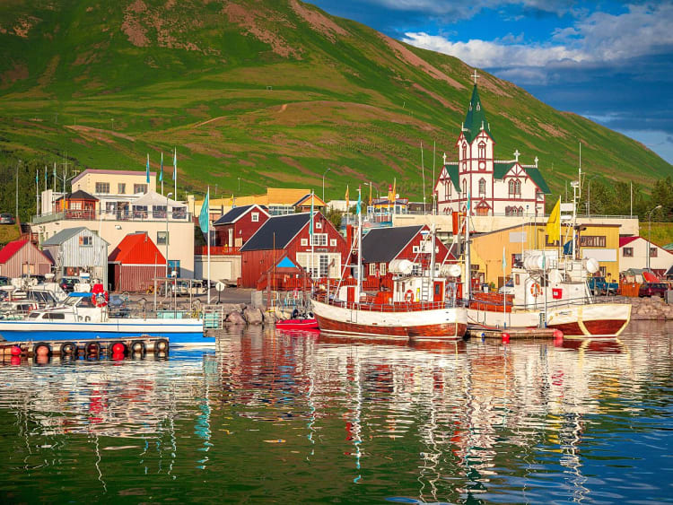 H&uacute;sav&iacute;ks Hafen im Abendlicht mit Fischerbooten, Holzkirche und sanften H&uuml;geln.