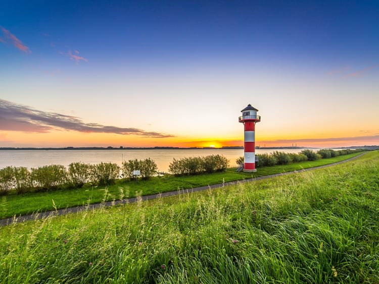 Rot-wei&szlig;er Leuchtturm am Wasser bei Sonnenuntergang an der Elbe