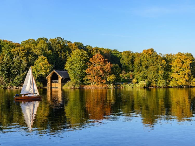 Kleines Segelboot vor herbstlich gef&auml;rbtem Uferwald an der Havel