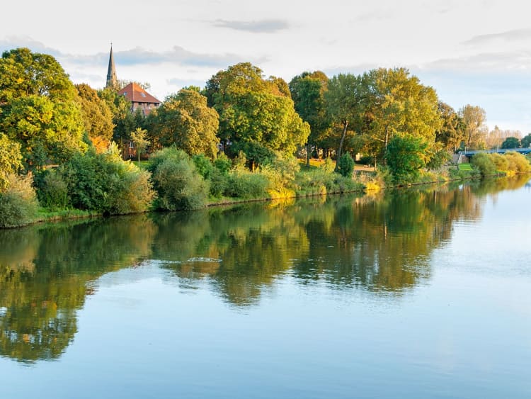Gr&uuml;ne B&auml;ume und Kirchturm spiegeln sich im ruhigen Wasser der Weser
