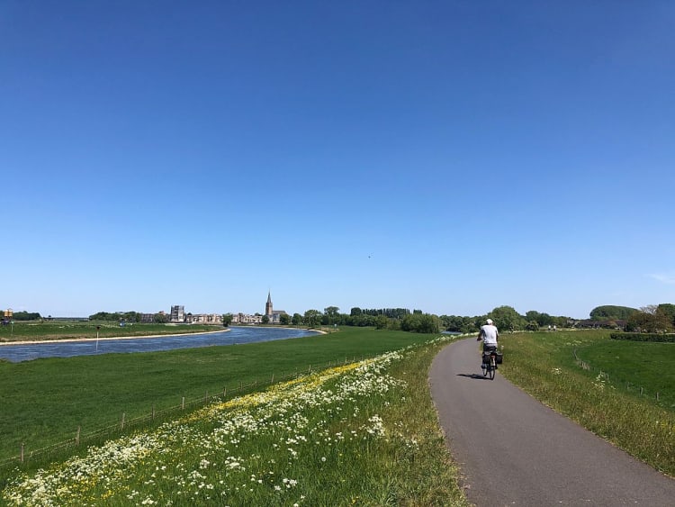 Radfahrer auf einem Deichweg entlang eines Flusses bei klarem Sommerhimmel