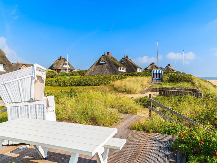 Sylt, Deutschland &ndash; Wei&szlig;er Strandkorb vor D&uuml;nen und reetgedeckten H&auml;usern am Meer