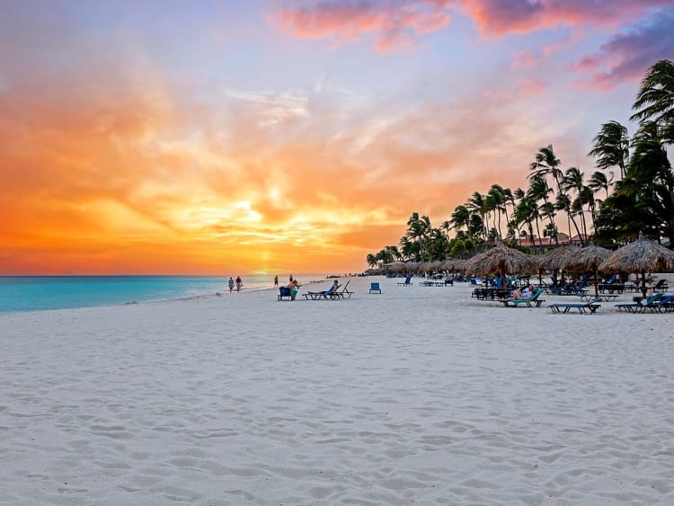Oranjestad, Aruba &ndash; leuchtender Sonnenuntergang &uuml;ber wei&szlig;em Sand und Palmen