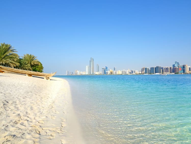 Abu Dhabi, VAE &ndash; wei&szlig;er Sandstrand vor t&uuml;rkisblauem Wasser und moderner Skyline