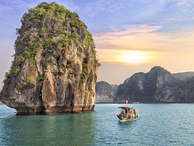 Halong, Vietnam &ndash; Fischerboot gleitet vor gewaltigem Felsen durch ruhige Abendbucht
