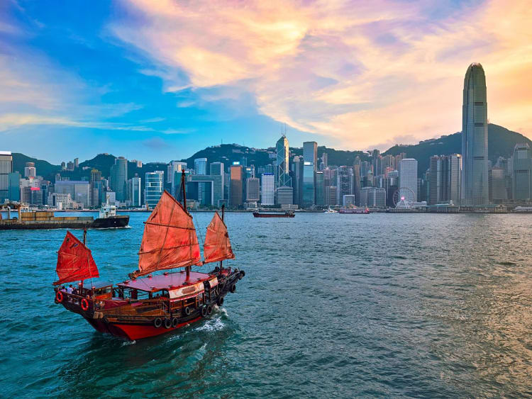Hongkong, China &ndash; Dschunke mit roten Segeln gleitet vor Skyline