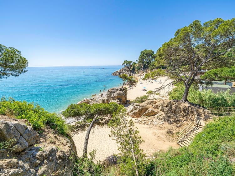 Palam&oacute;s, Spanien - Helle Sandbucht mit Felszugang und Kiefernschatten am Wasser