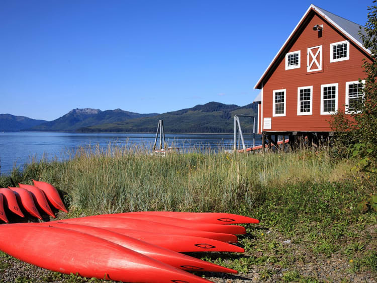Icy Strait Point, USA &ndash; Rotes Holzhaus am Ufer mit roten Kajaks im Vordergrund