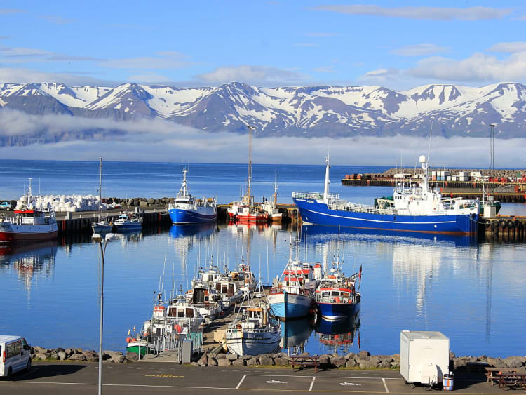 Akureyri, Island - Bunte Schiffe im klaren Wasser mit Bergkulisse im Hintergrund