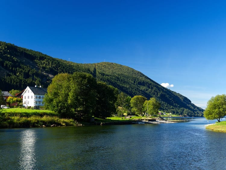Eidsfjord, Norwegen - Wei&szlig;es Haus am ruhigen Fluss mit bewaldetem Berghang
