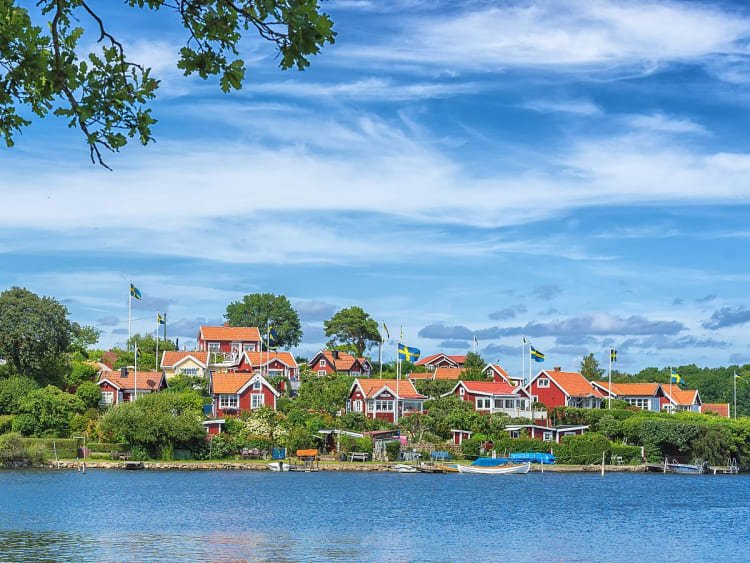 Karlskrona, Schweden &ndash; rote Holzh&auml;user mit schwedischen Flaggen am Ufer