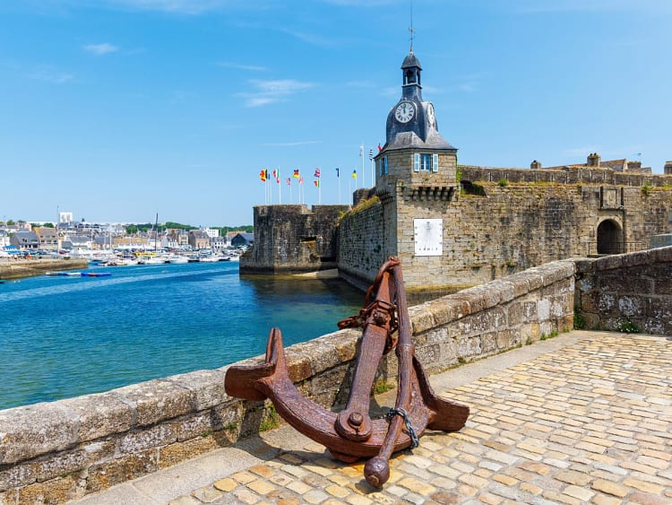 Concarneau, Frankreich &ndash; Historische Festungsmauern mit Uhrturm und gro&szlig;em Anker am Hafen