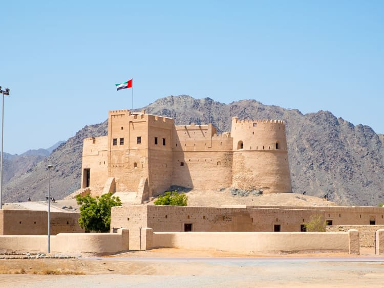 Fujairah, VAE &ndash; Historisches Fujairah Fort mit Landesflagge vor Gebirgskulisse