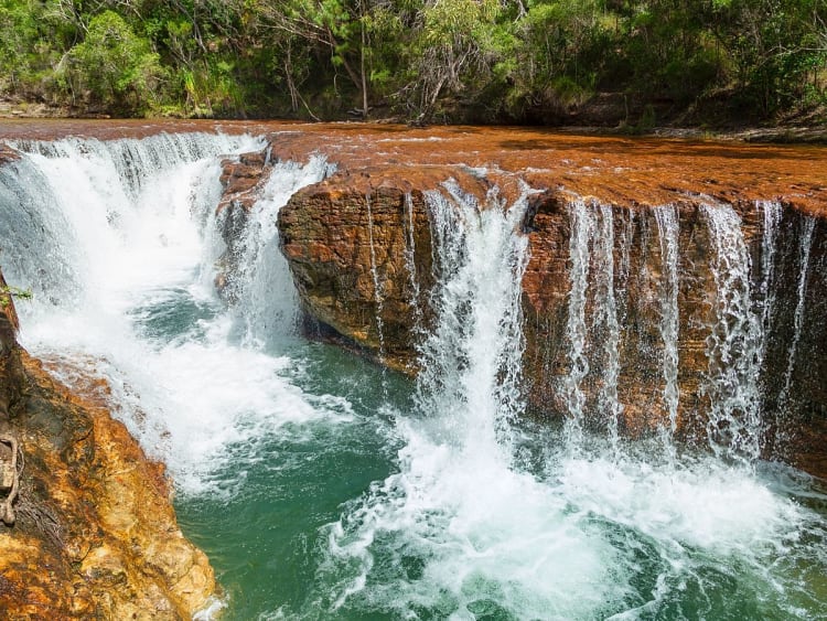 Cape York, Australien &ndash; Kleiner Wasserfall &uuml;ber r&ouml;tliche Felsen in tropischer Natur