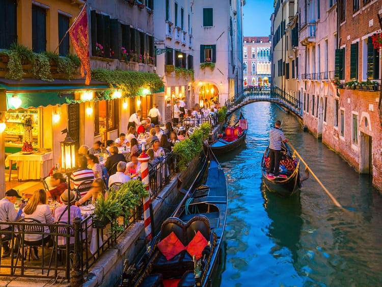Venedig, Italien &ndash; Abendszene mit belebtem Restaurant am Kanal und vorbeifahrender Gondel