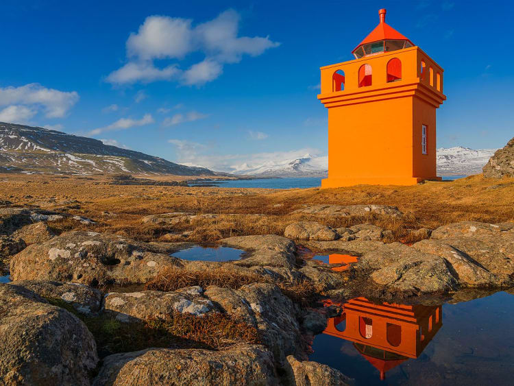Dj&uacute;pivogur, Island &ndash; Farbintensiver Leuchtturm spiegelt sich in Wasserpf&uuml;tzen auf felsigem Boden