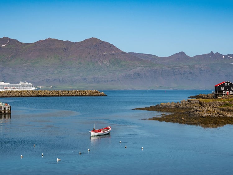 Dj&uacute;pivogur, Island &ndash; Hafen mit kleinem Boot, Kreuzfahrtschiff und Bergen im Hintergrund
