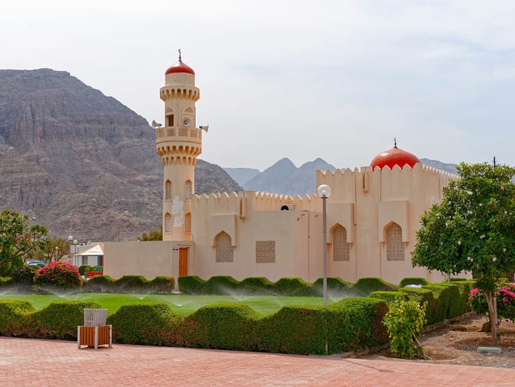 Khasab, Oman &ndash; Wei&szlig;e Moschee mit roter Kuppel und gepflegtem Garten vor Gebirgskulisse