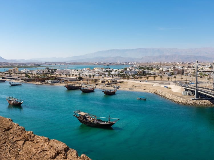 Sur, Oman &ndash; Fischerboote im ruhigen Hafenbecken mit Stadt und Bergen im Hintergrund