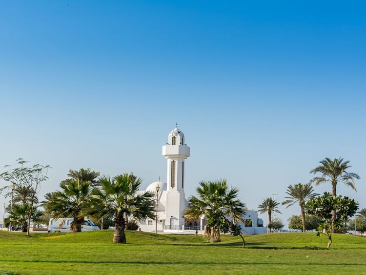 Dammam, Saudi-Arabien &ndash; Kleine wei&szlig;e Moschee mit Minarett inmitten gr&uuml;ner Palmenlandschaft