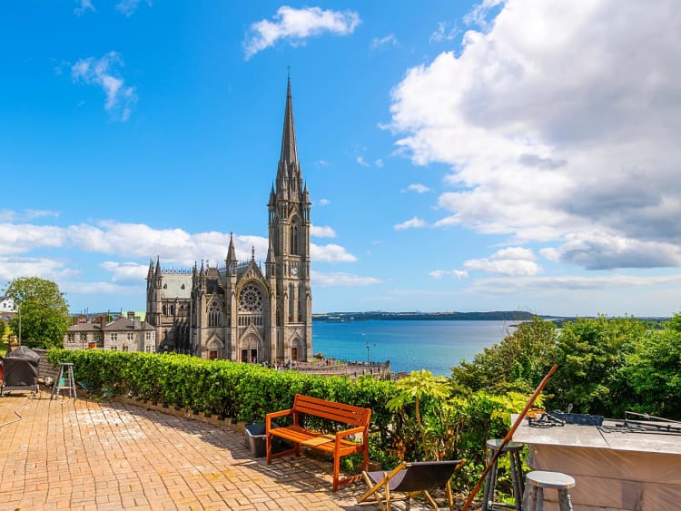 Cobh, Irland &ndash; St. Colman&rsquo;s Cathedral mit Blick auf den Hafen und das Meer bei blauem Himmel