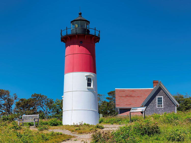 Falmouth, England &ndash; Rot-wei&szlig;er Leuchtturm vor klarem blauen Himmel neben einem kleinen H&auml;uschen