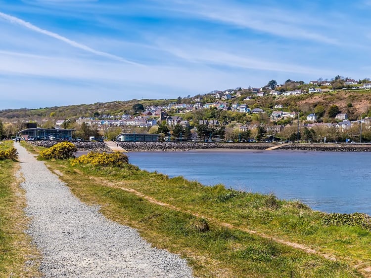 Fishguard, Wales &ndash; Spazierweg am Wasser mit Blick auf die h&uuml;gelige Stadtlandschaft im Sonnenschein