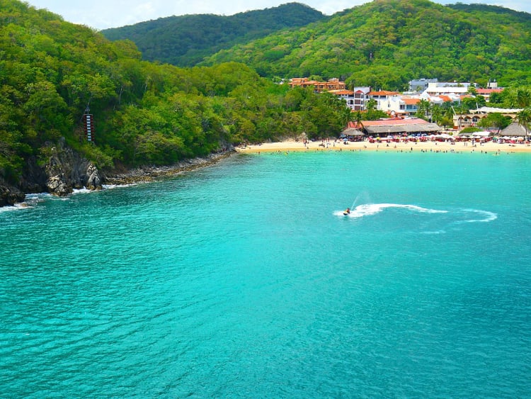 Huatulco, Mexiko &ndash; t&uuml;rkisfarbene Bucht mit Jet-Ski vor dicht bewachsenem Hang